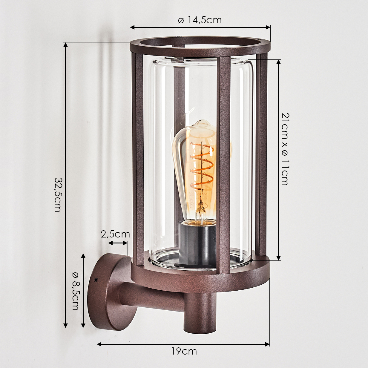 Eine braune Wandlampe mit Maßen. Eine Glasröhre mit Glühbirne wird von einem Metallrahmen geschützt. Sie ist an einer weißen Wand befestigt.