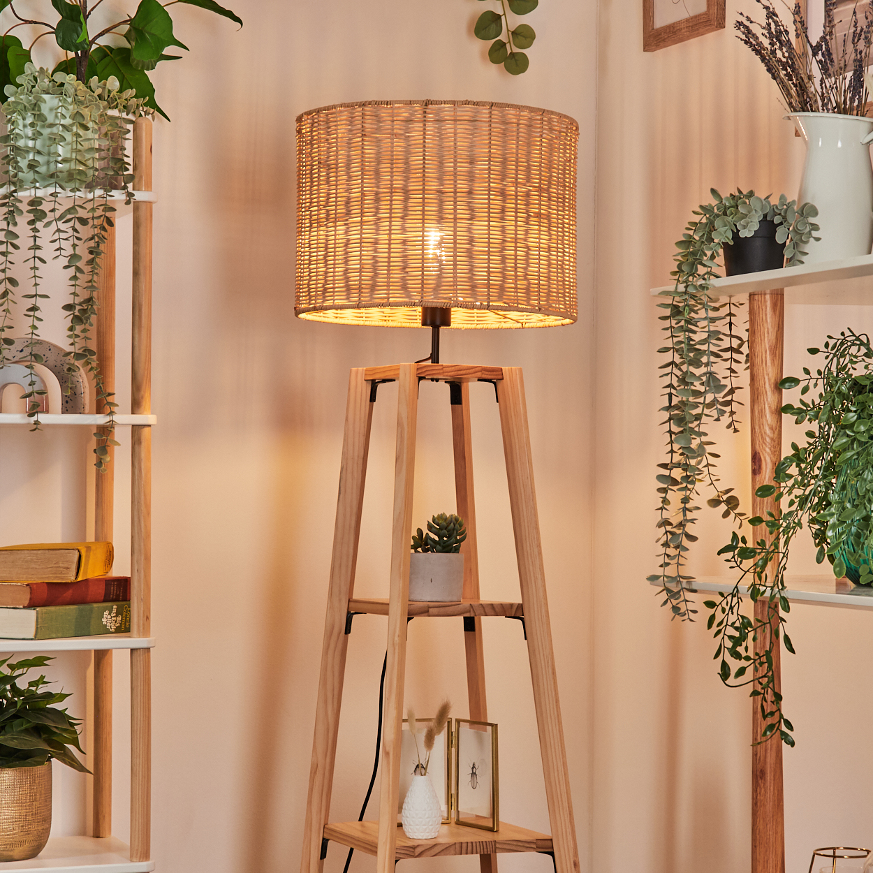 Eine gewebte Lampe steht auf einem Holzständer mit Regalen. Pflanzen schmücken die Szene; einige hängen, andere in Töpfen, schaffen eine gemütliche Atmosphäre.