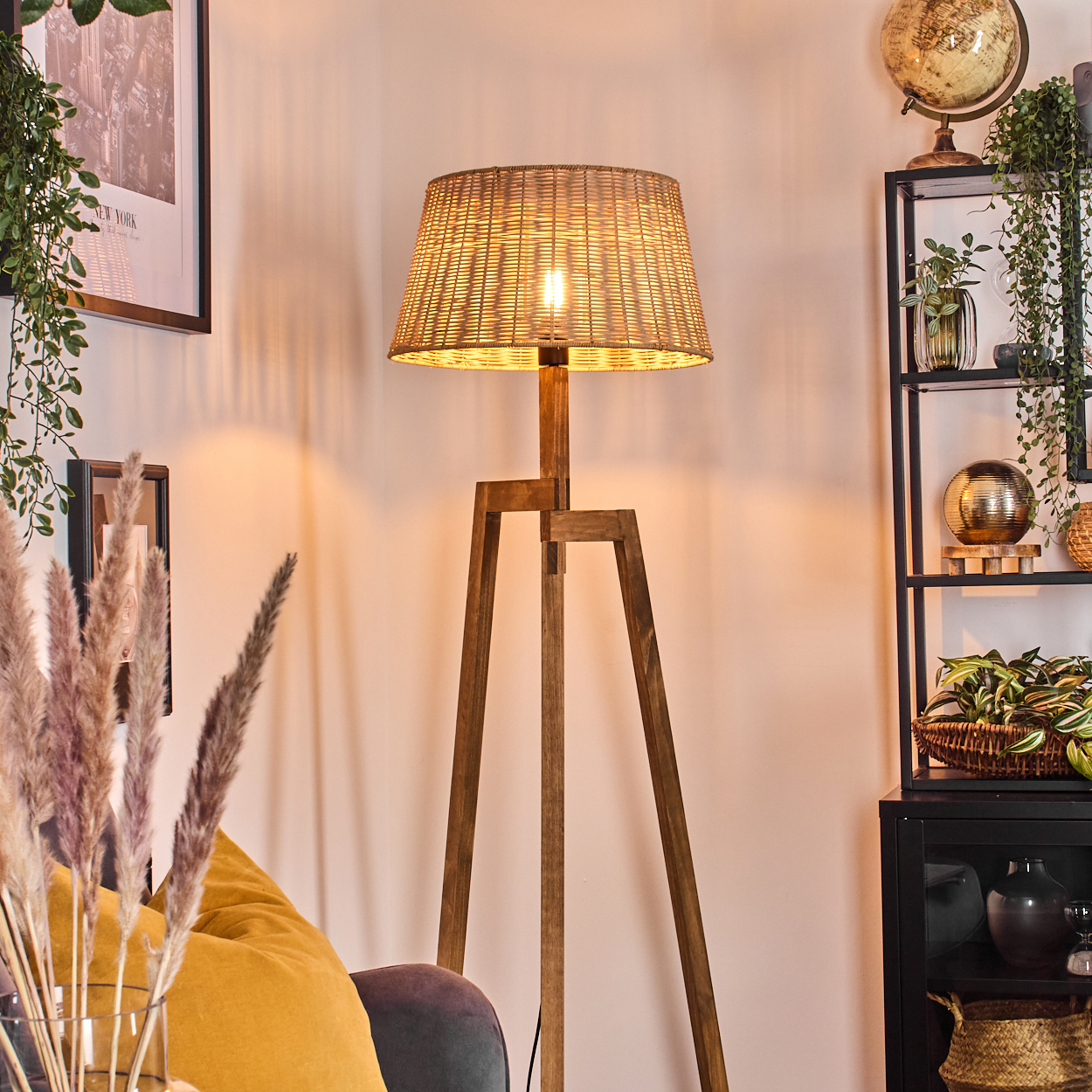 Eine Stehlampe aus Holz mit einem gewebten Lampenschirm steht in einem Raum. Ein Regal mit Dekor und Pflanzen befindet sich rechts.