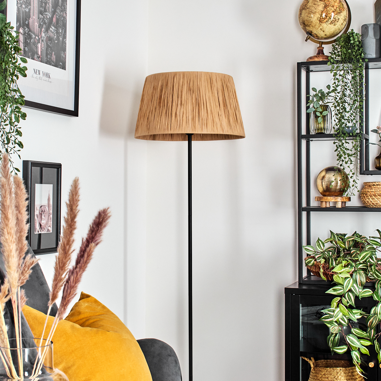 Raumecke mit Stehlampe, Regal mit Deko und Sofa. Die Lampe hat einen beigen Schirm. Das Regal enthält Pflanzen und einen Globus.