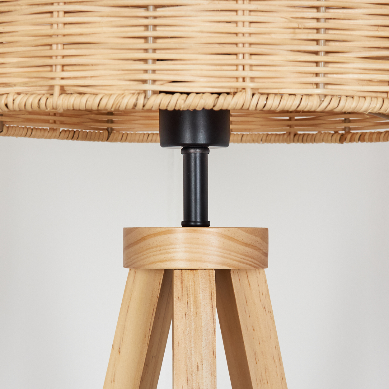 Nahaufnahme einer Lampe mit gewebtem Lampenschirm, schwarzem Schaft und Holzstativfuß vor weißem Hintergrund.