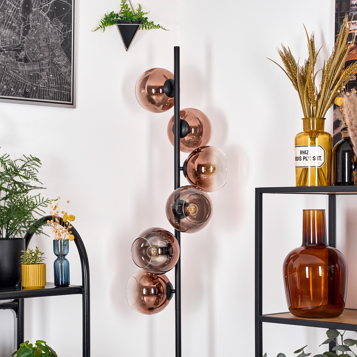 Modernes Wohnzimmer mit schwarzer Stehlampe mit Glaskugeln. Regale mit Vasen und Pflanzen sowie ein Kartenbild.