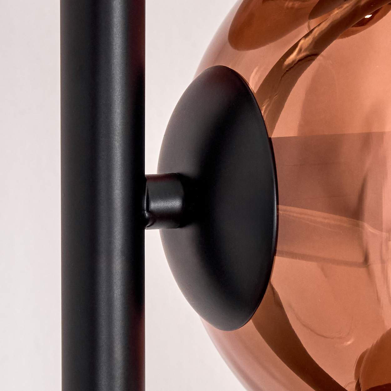 Nahaufnahme einer Lampe. Schwarzer Metallschaft und kreisförmiger Sockel tragen eine kupferfarbene Glaskugel auf weißem Hintergrund.