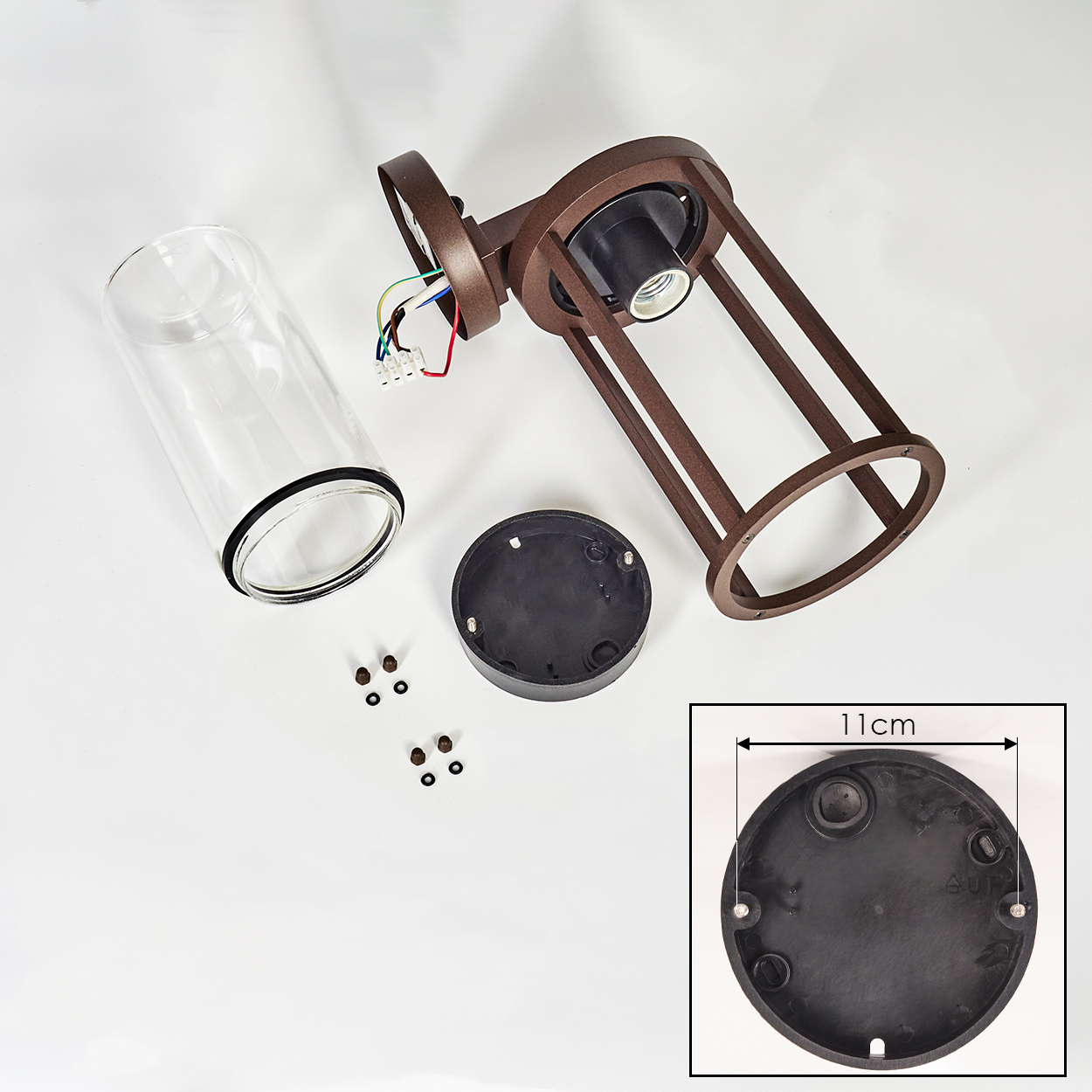 Zerlegte braune Lampe mit Glaszylinder, schwarzem Sockel und Kleinteilen auf weißer Oberfläche. Eine Einlage zeigt die Sockelmaße.