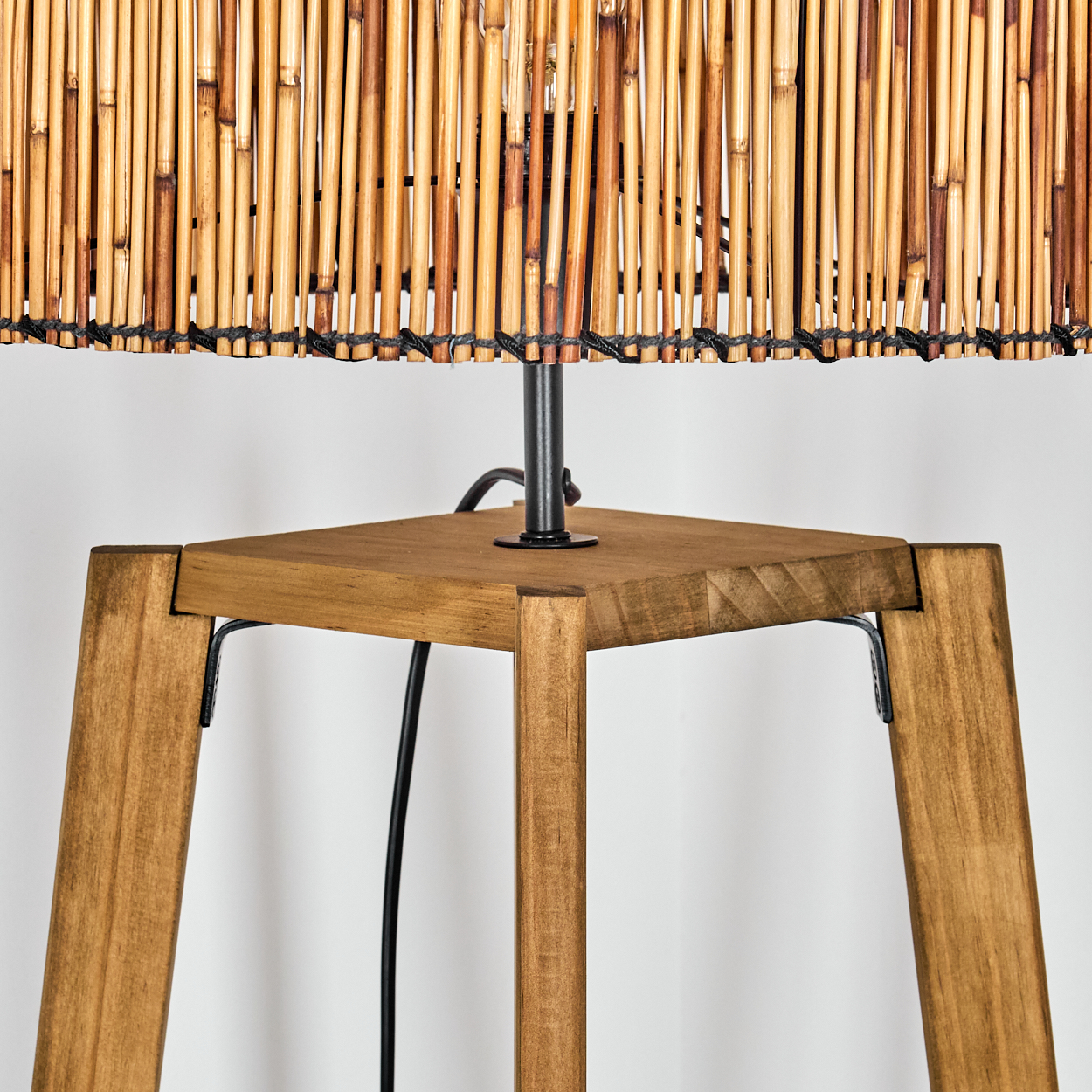 Nahaufnahme einer Lampe mit Bambus-Lampenschirm und Holzbeinen. Ein schwarzes Kabel und Metallelemente sind sichtbar.