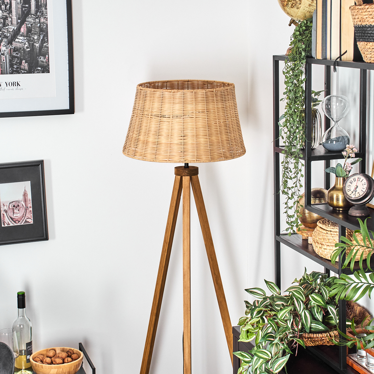 Ein gewebter Lampenschirm auf einem Holzstativ. Ein Bücherregal enthält Dekoration, und ein gerahmter New York-Druck hängt an der Wand.