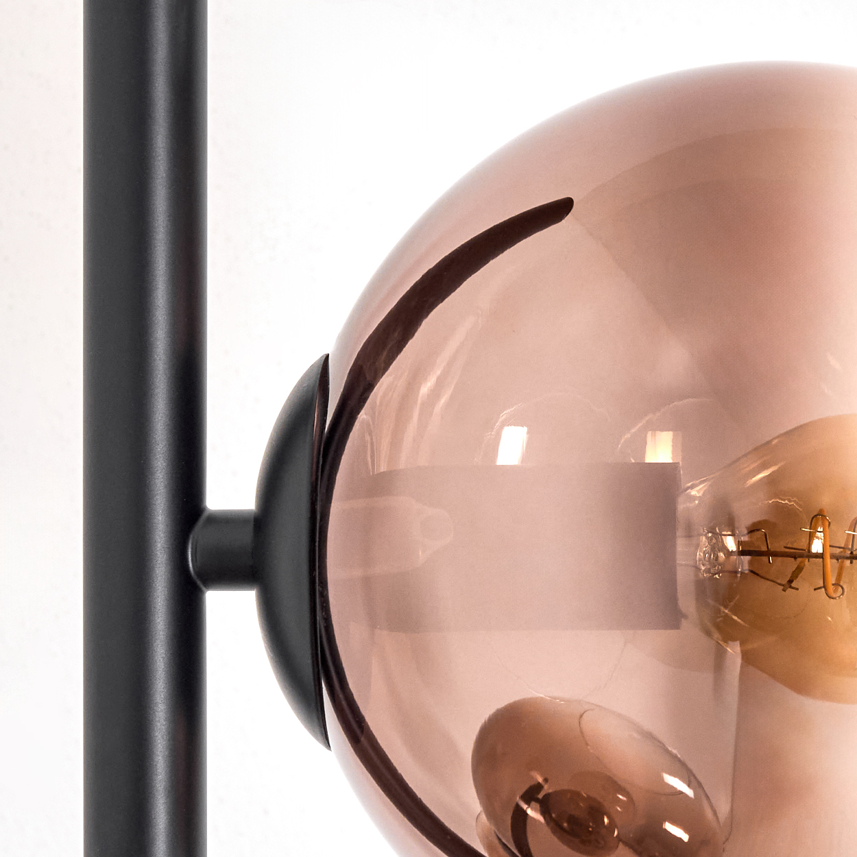 Nahaufnahme einer Lampe. Ein schwarzer Metallrahmen trägt eine rosafarbene Glaskugel mit einer sichtbaren Glühbirne.