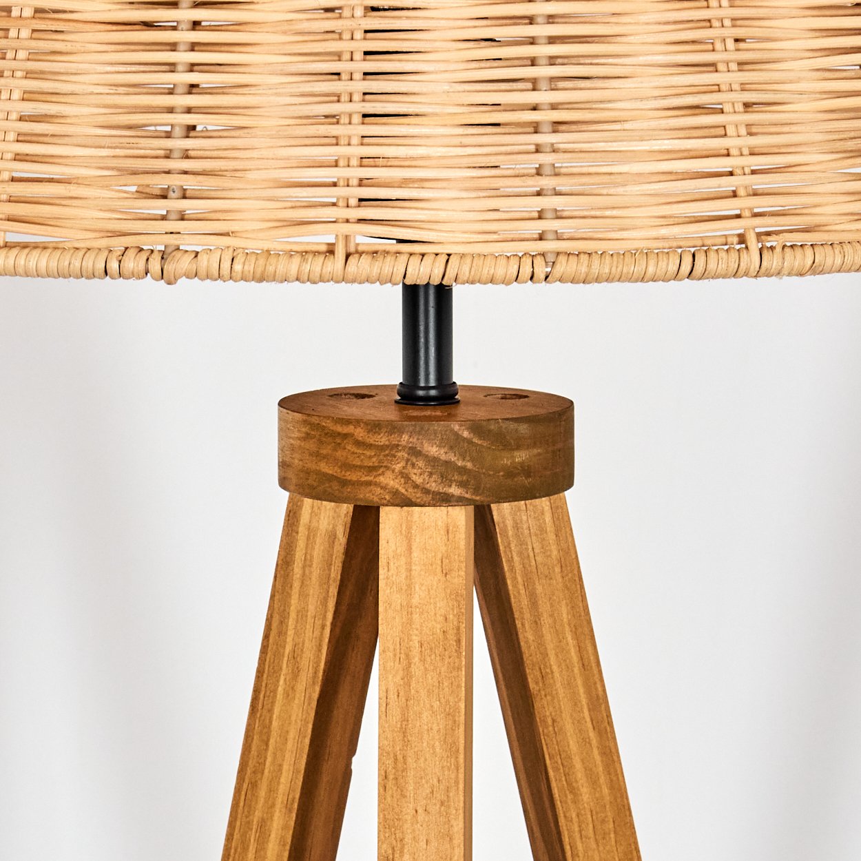 Nahaufnahme einer Lampe. Sie hat einen gewebten Lampenschirm, ein Holzstativ und eine schwarze Metallstange.