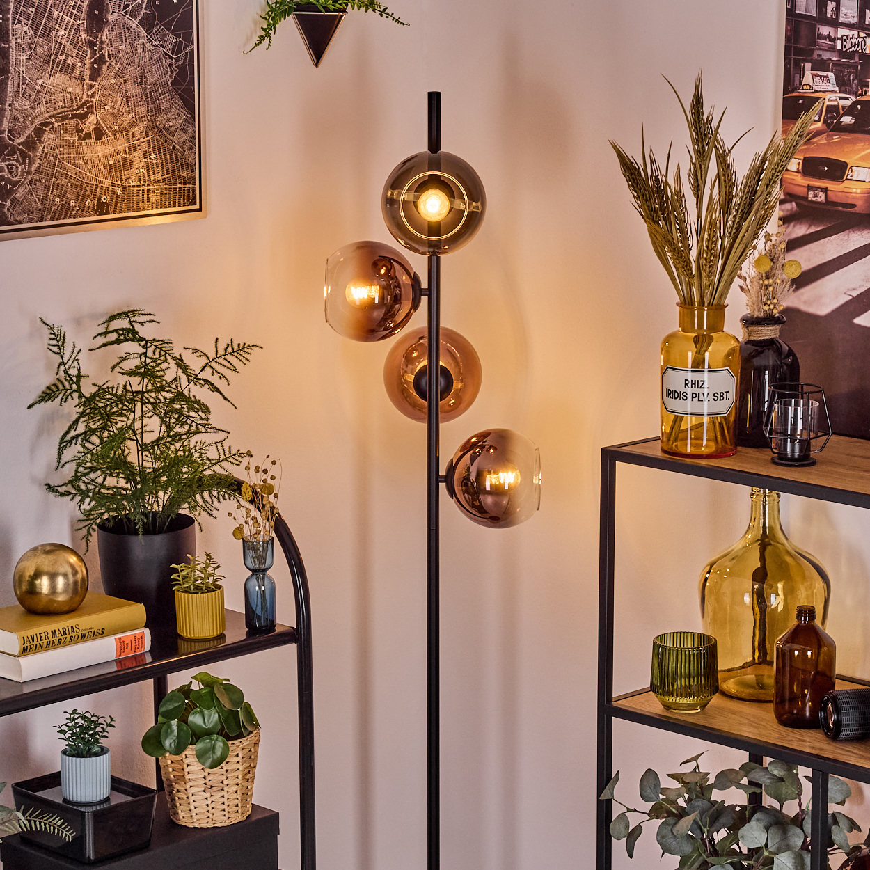 Ein modernes Wohnzimmer mit einer schwarzen Stehlampe mit Glaskugeln, Pflanzen, Regalen und einem Kartenbild an der Wand.