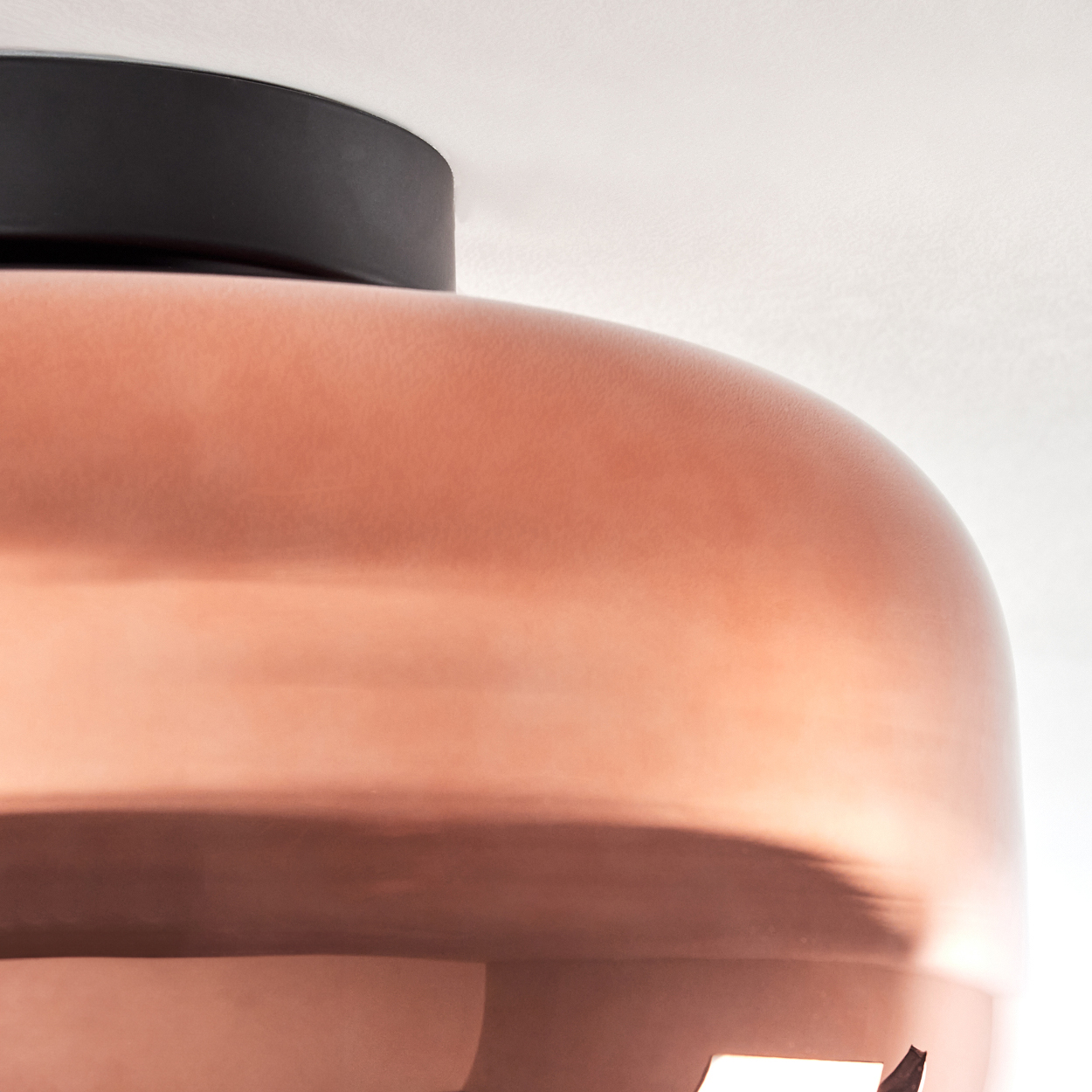 Nahaufnahme einer kupferfarbenen Pendelleuchte. Die Lampe hat eine schwarze Oberseite und eine glatte, abgerundete Form. Der Hintergrund ist weiß.