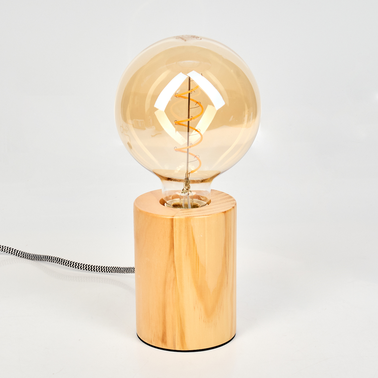 Eine dekorative Lampe mit einer großen, runden bernsteinfarbenen Glühbirne auf einem zylindrischen Holzsockel. Ein schwarz-weißes Netzkabel ist angebracht.