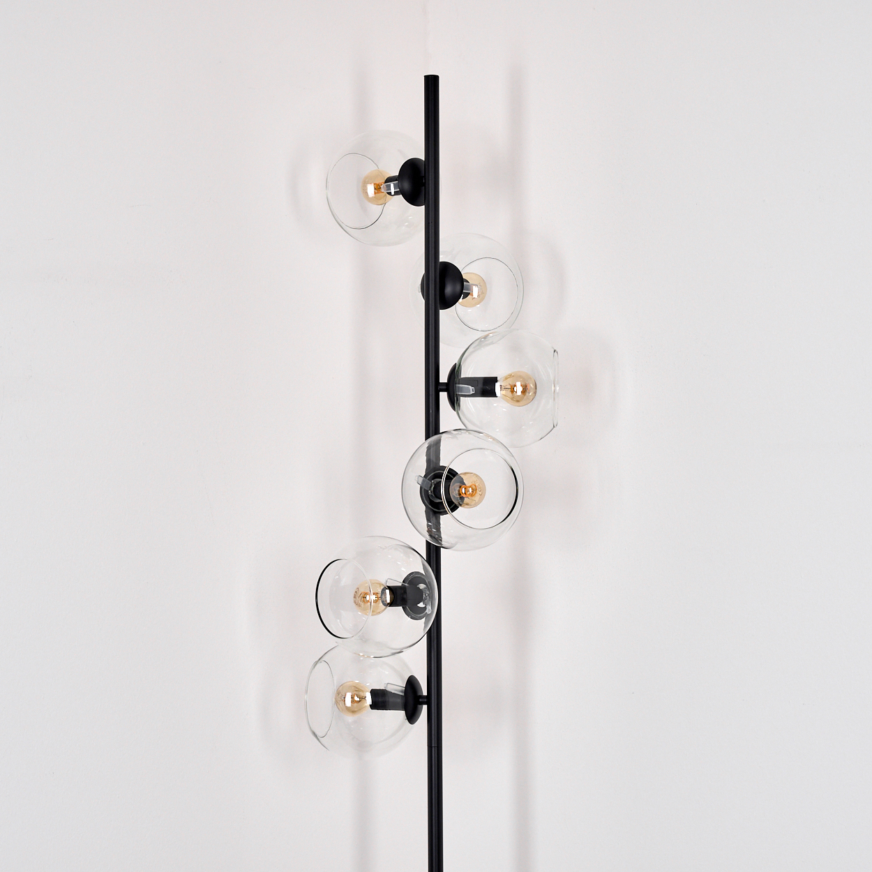 Eine moderne Wandlampe mit fünf klaren Glaskugeln, in denen sich jeweils eine Glühbirne befindet, an einer schwarzen, vertikalen Stange.