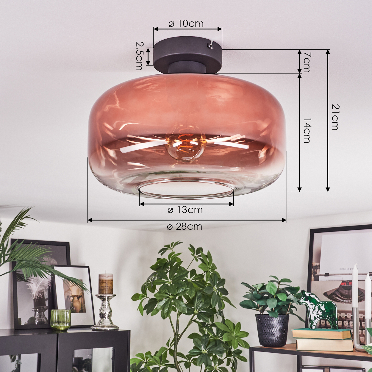 Gezeigt wird eine rosafarbene Deckenlampe aus Glas. Maße sind beschriftet. Der Hintergrund umfasst Pflanzen, Kerzen und Bilder.