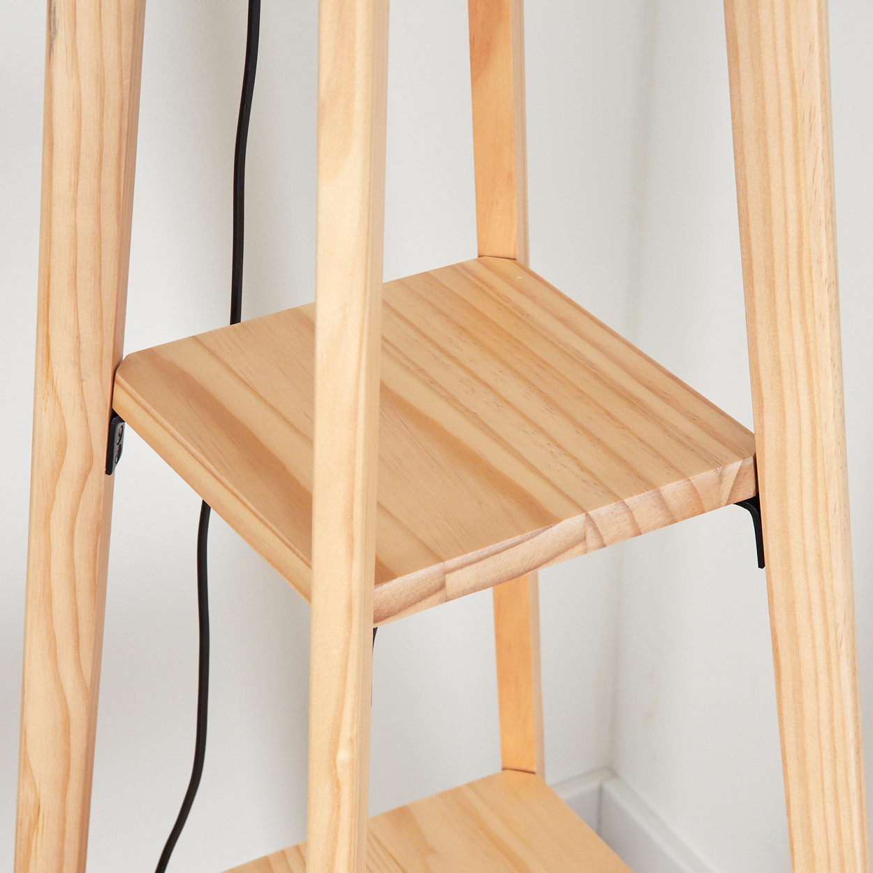 Holzregal mit zwei Ebenen. Ein schwarzes Kabel ist sichtbar. Der Hintergrund ist eine weiße Wand. Das Holz ist hell.