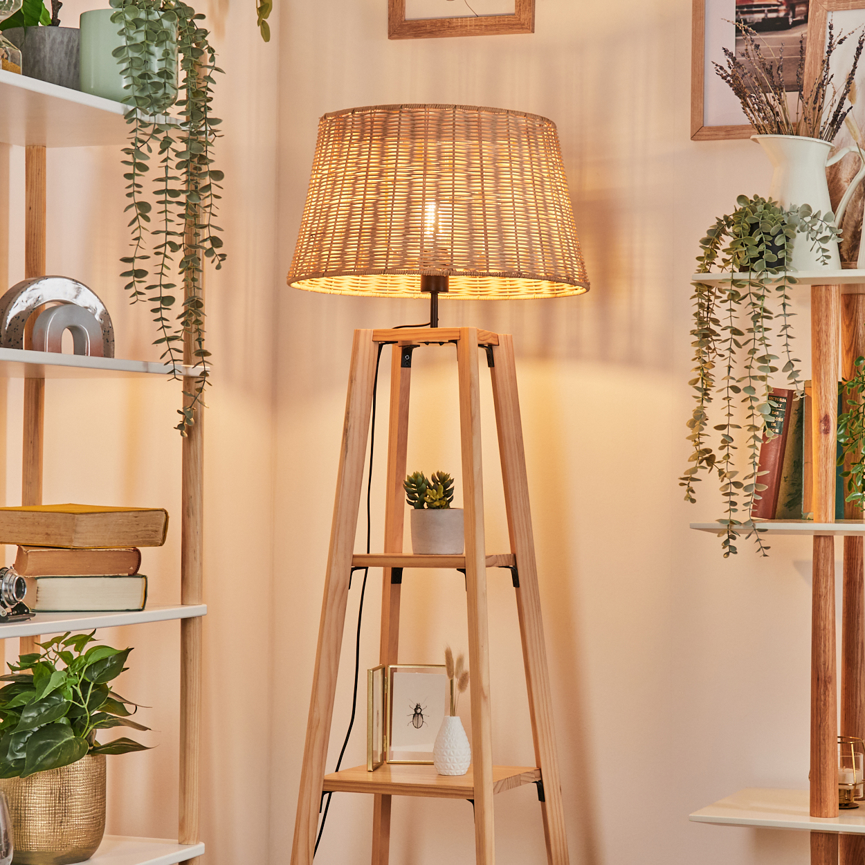 Eine gewebte Lampe mit Holzständer steht in einem Raum. Regale mit Pflanzen und Büchern befinden sich auf beiden Seiten der Lampe.