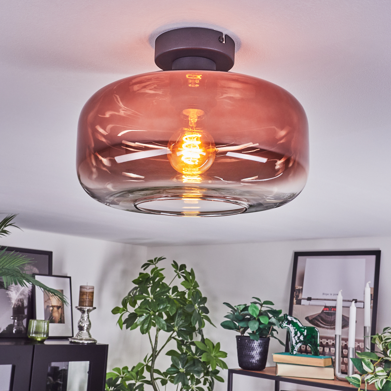 Eine moderne Deckenlampe mit rosafarbenem Glasschirm. Die Szene umfasst Pflanzen, Bilder und andere Dekorationsgegenstände in einem Raum.
