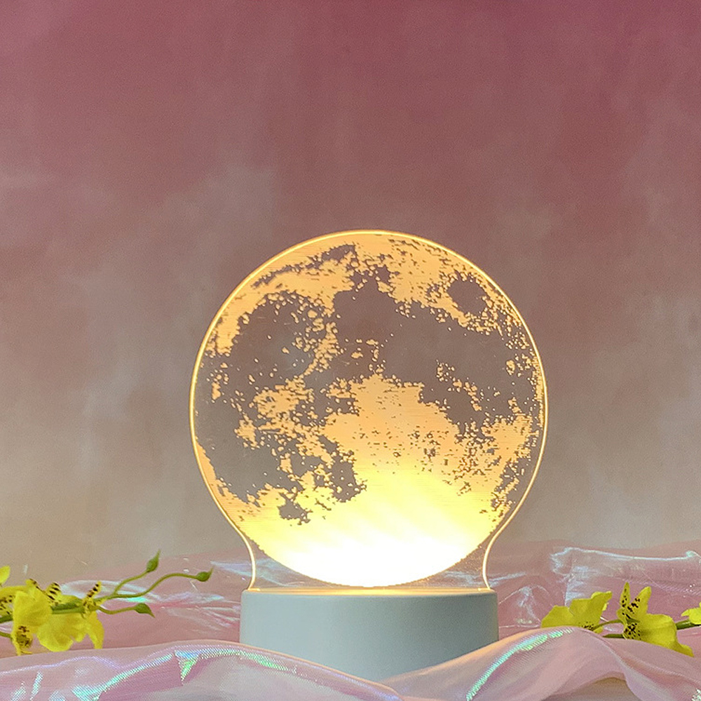 Eine leuchtende mondförmige Lampe auf einem weißen Sockel. Rosa Hintergrund mit Blumen und schillerndem Stoff.