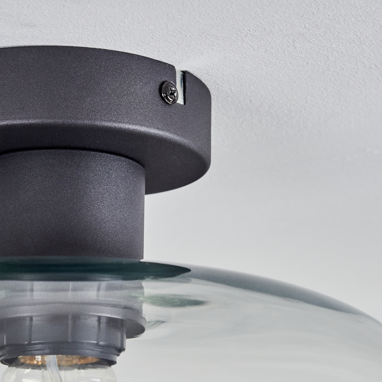 Nahaufnahme einer schwarzen Deckenlampe. Die Lampe hat einen Glasschirm und ist an einer weißen Decke montiert.