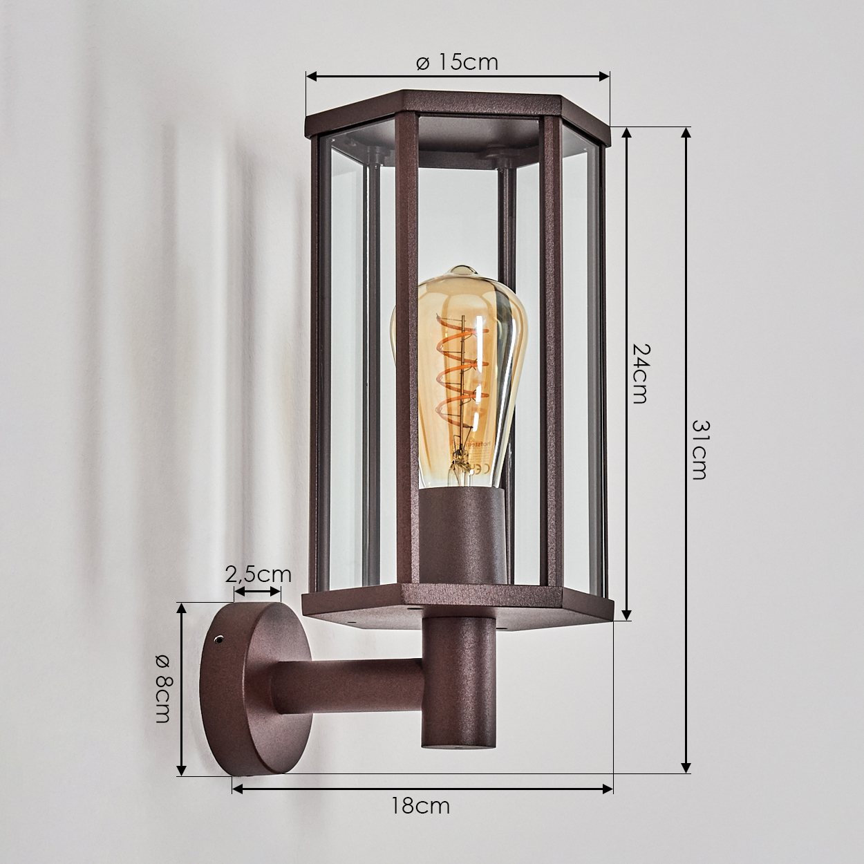 Eine bronzefarbene Außenwandleuchte. Sie hat ein rechteckiges Glasgehäuse um eine Glühbirne. Abmessungen sind beschriftet: 15 cm, 24 cm, 31 cm, 8 cm, 2,5 cm, 18 cm.