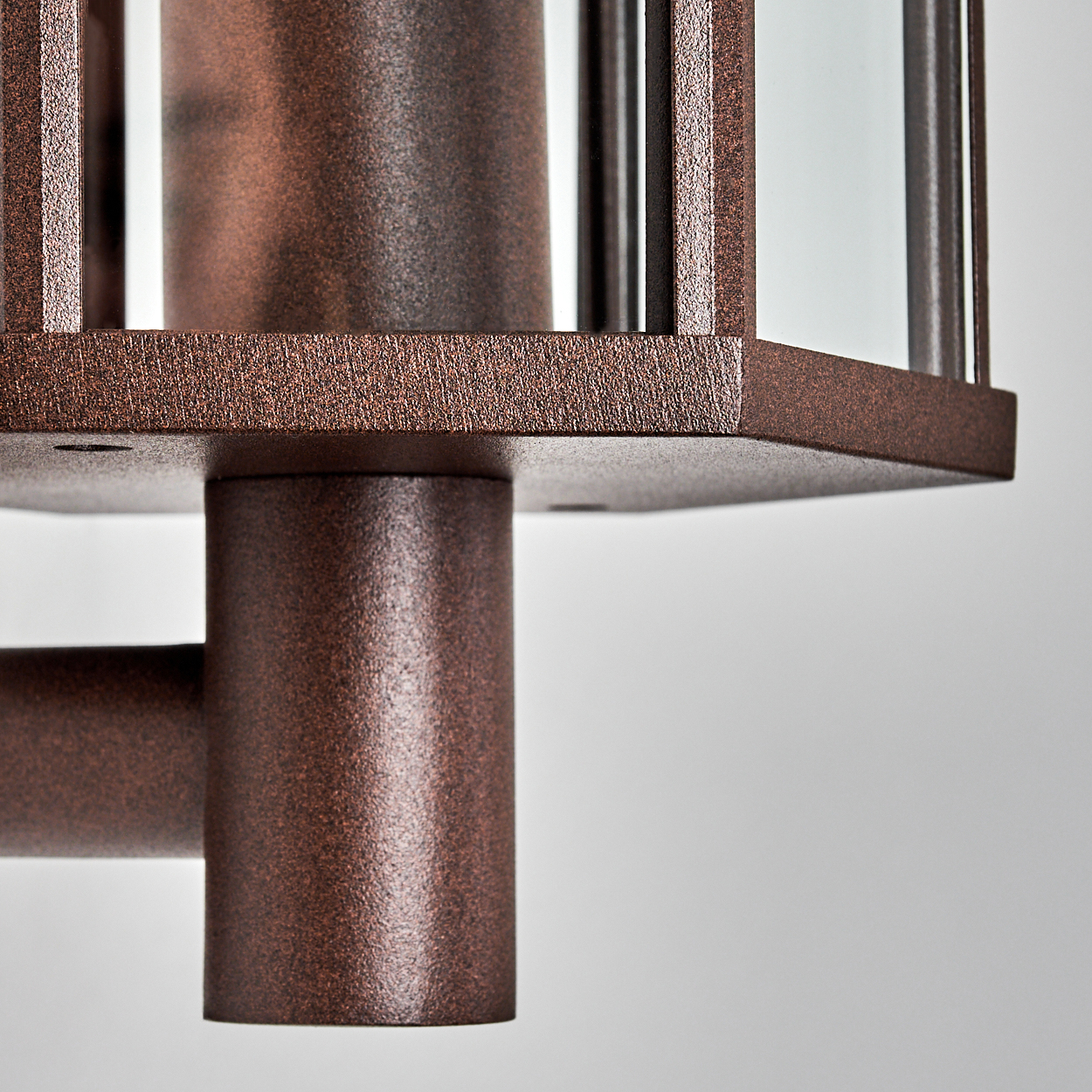 Nahaufnahme einer bronzefarbenen Außenlampe. Die Lampe hat einen zylindrischen Sockel und eine quadratische Oberseite mit Glasscheiben. Weißer Hintergrund.