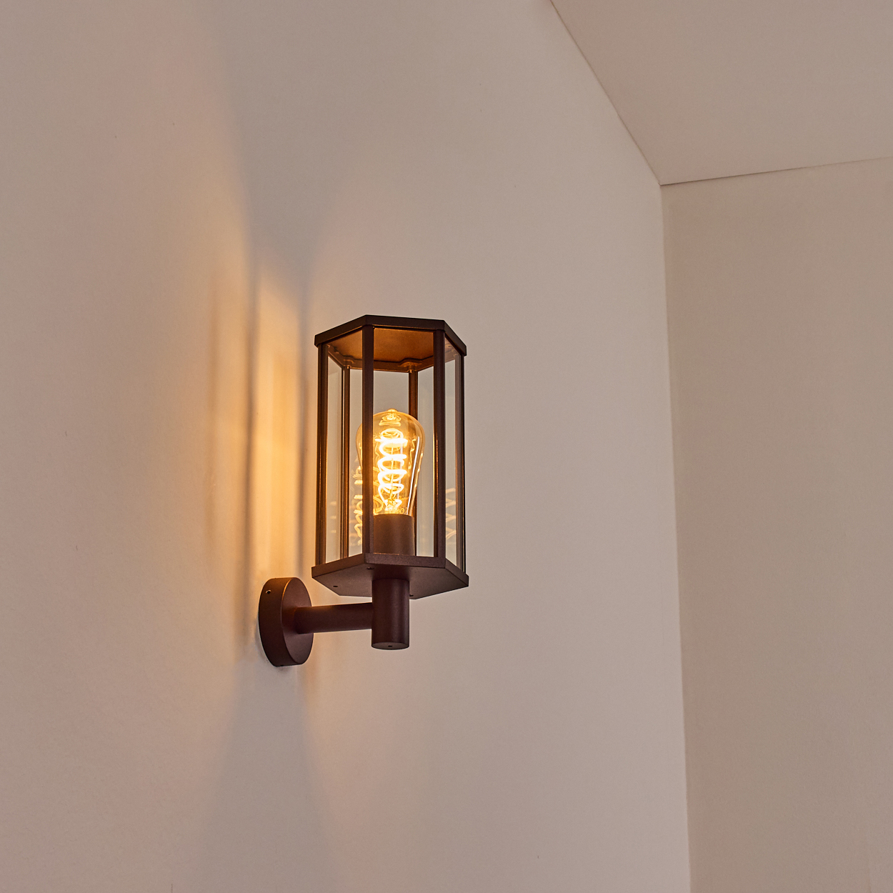 Eine an der Wand montierte schwarze Leuchte mit einer glühenden Glühbirne. Sie befindet sich an einer weißen Wand.