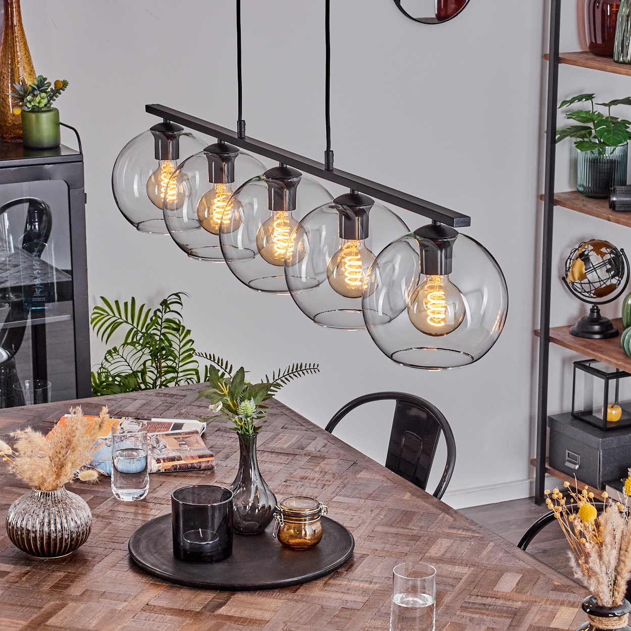 Ein Esszimmer mit Holztisch, Leuchte mit Kugelleuchten und verschiedenen Dekorationsartikeln.