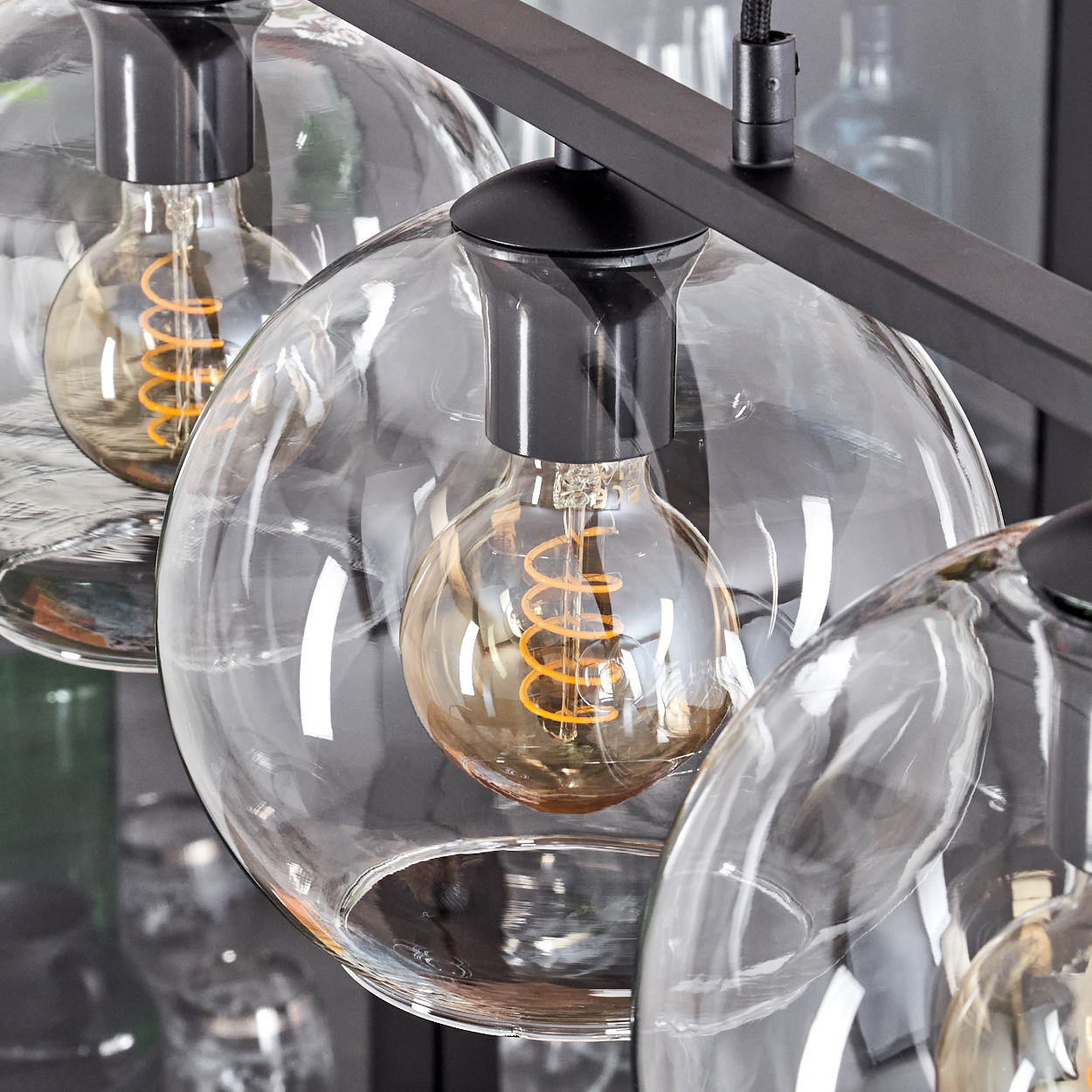 Nahaufnahme einer modernen Leuchte mit klaren Glaskugeln und Edison-Glühbirnen. Die Leuchte hat einen schwarzen Metallrahmen.