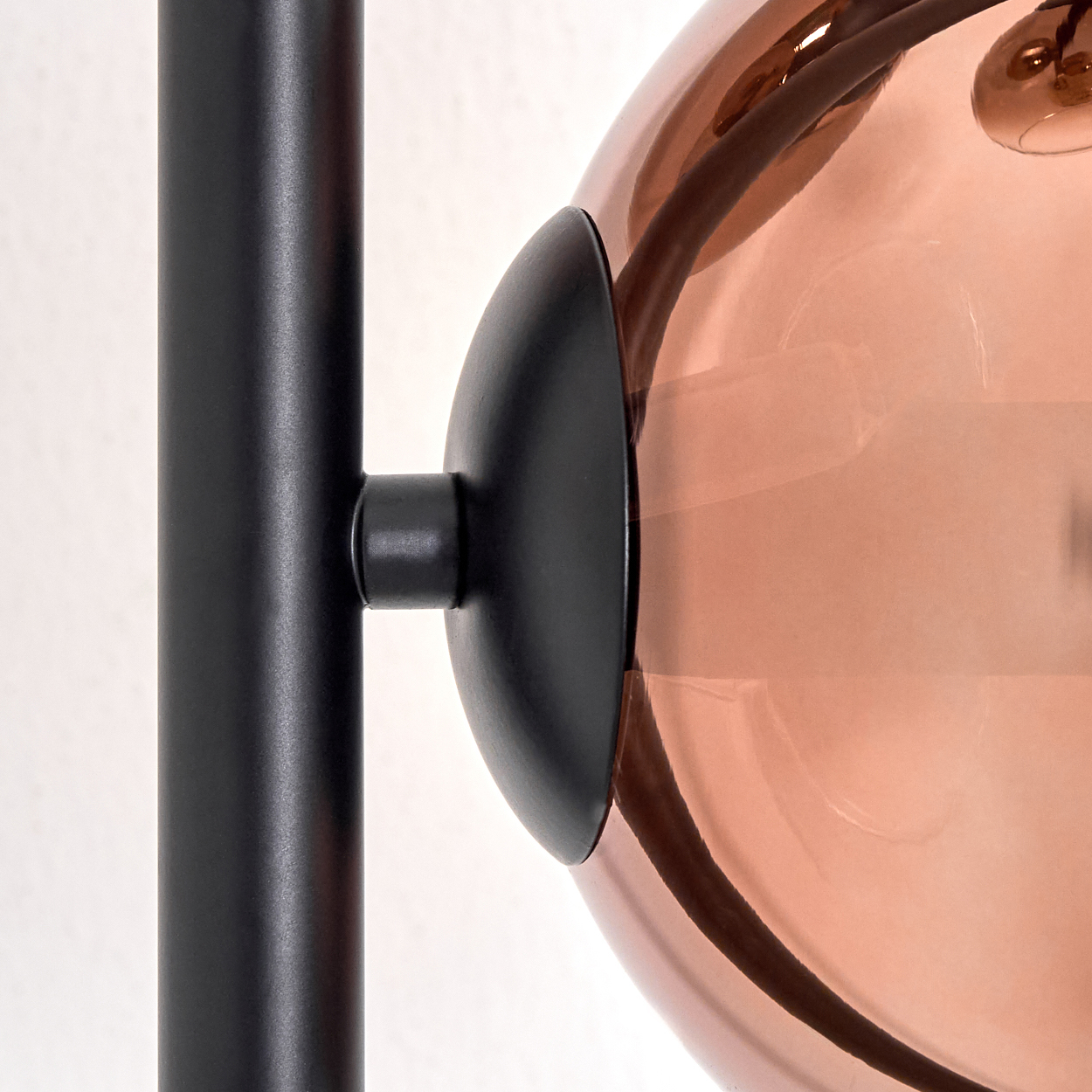 Nahaufnahme einer Lampe. Schwarzer Metallschaft und Halterung tragen eine große, durchscheinende, kupferfarbene Glaskugel. Weißer Hintergrund.