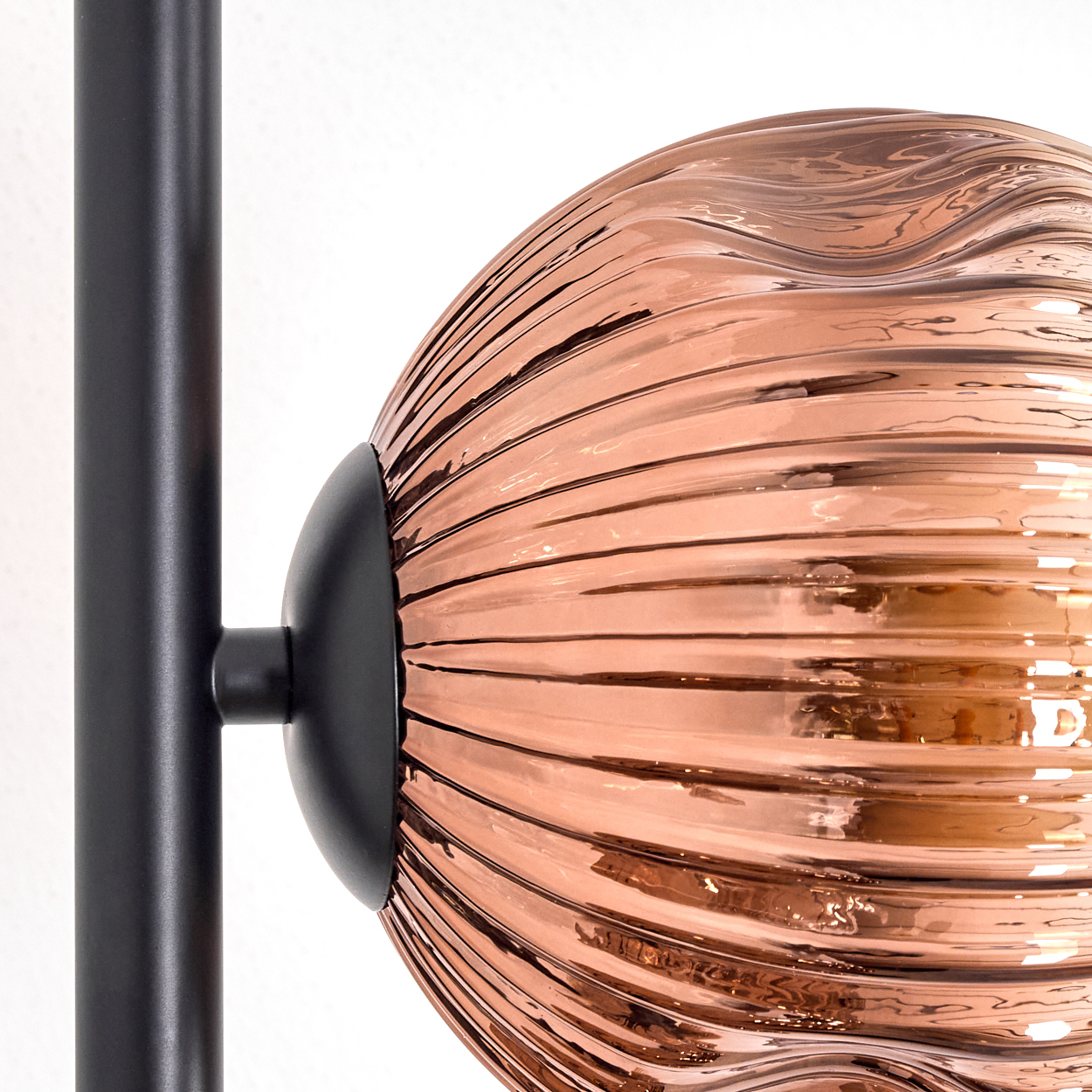 Nahaufnahme einer Lampe. Sie hat eine kupferfarbene, gerippte Glaskugel, die an einem schwarzen Metallrahmen befestigt ist.
