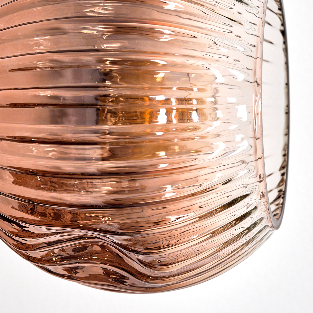 Nahaufnahme eines klaren Glasobjekts mit welliger, geriffelter Oberfläche. Das Glas ist mit einem warmen, bernsteinfarbenen Farbton versehen. Weißer Hintergrund.