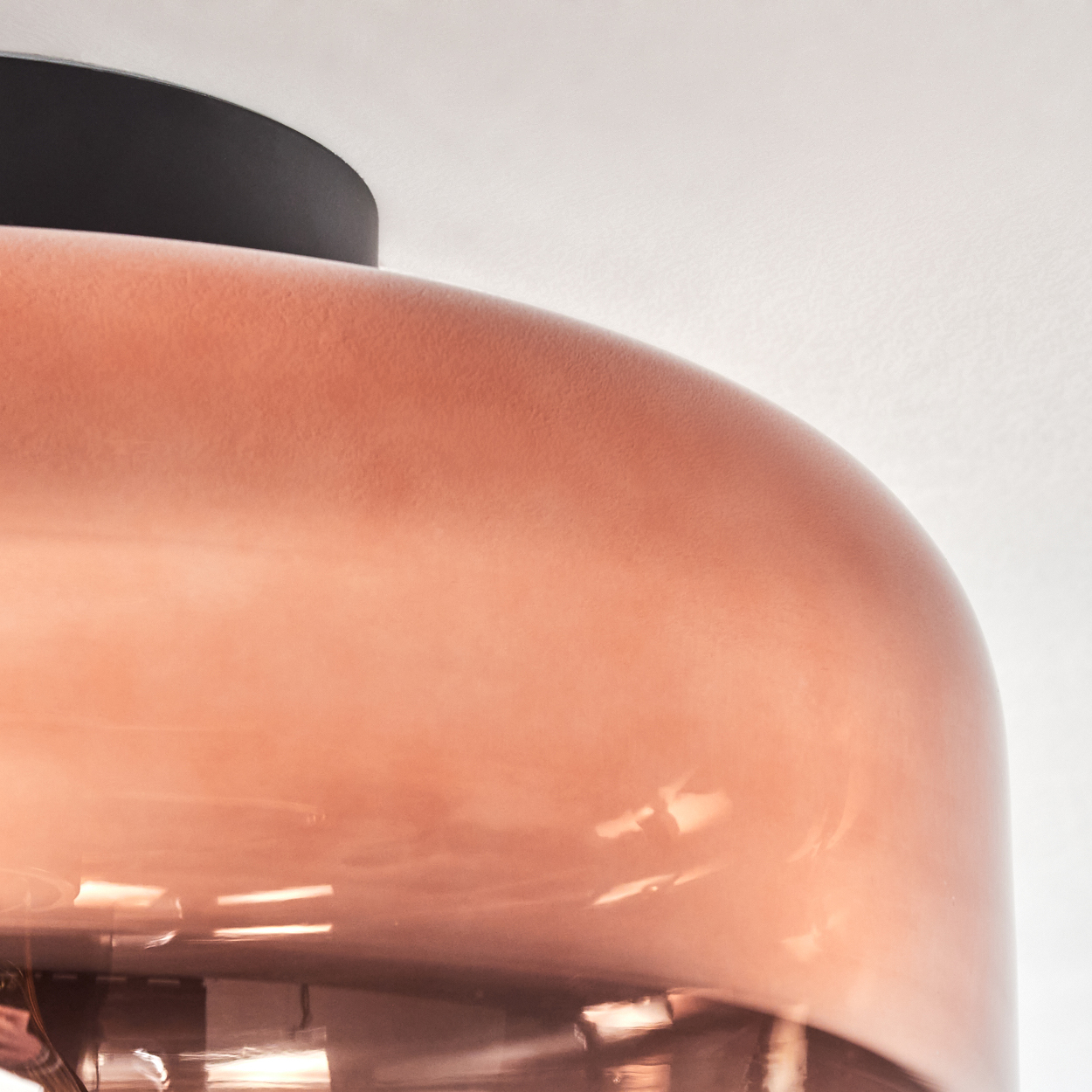 Nahaufnahme eines kupferfarbenen Lampenschirms. Schwarze Deckenleuchte darüber. Weißer Hintergrund. Die Lampe ist glänzend.