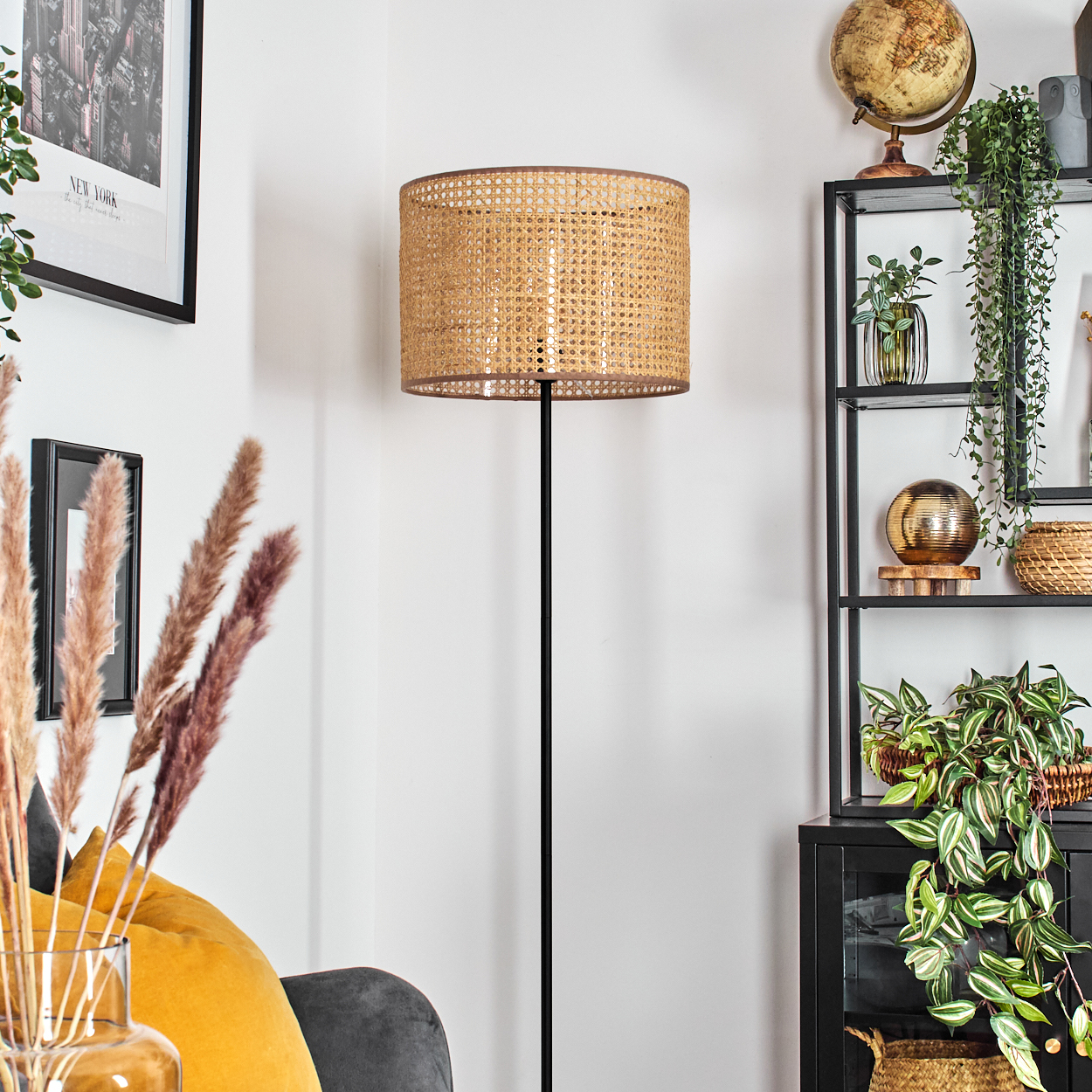 Ein Raum mit einer Lampe, einem Regal mit Dekorationen und einer Vase mit Pflanzen. Die Lampe hat einen gewebten Schirm.