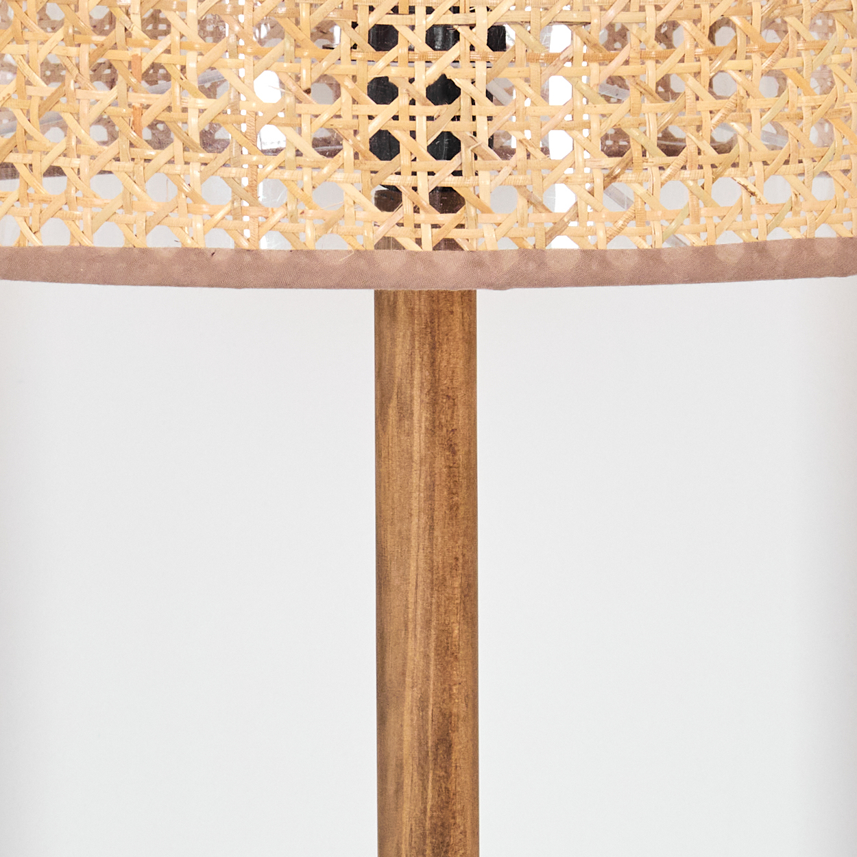 Nahaufnahme einer Lampe. Gewebter Schirm mit braunem Besatz, Holzstange und weißem Hintergrund. Der Schirm hat ein gewebtes Muster.