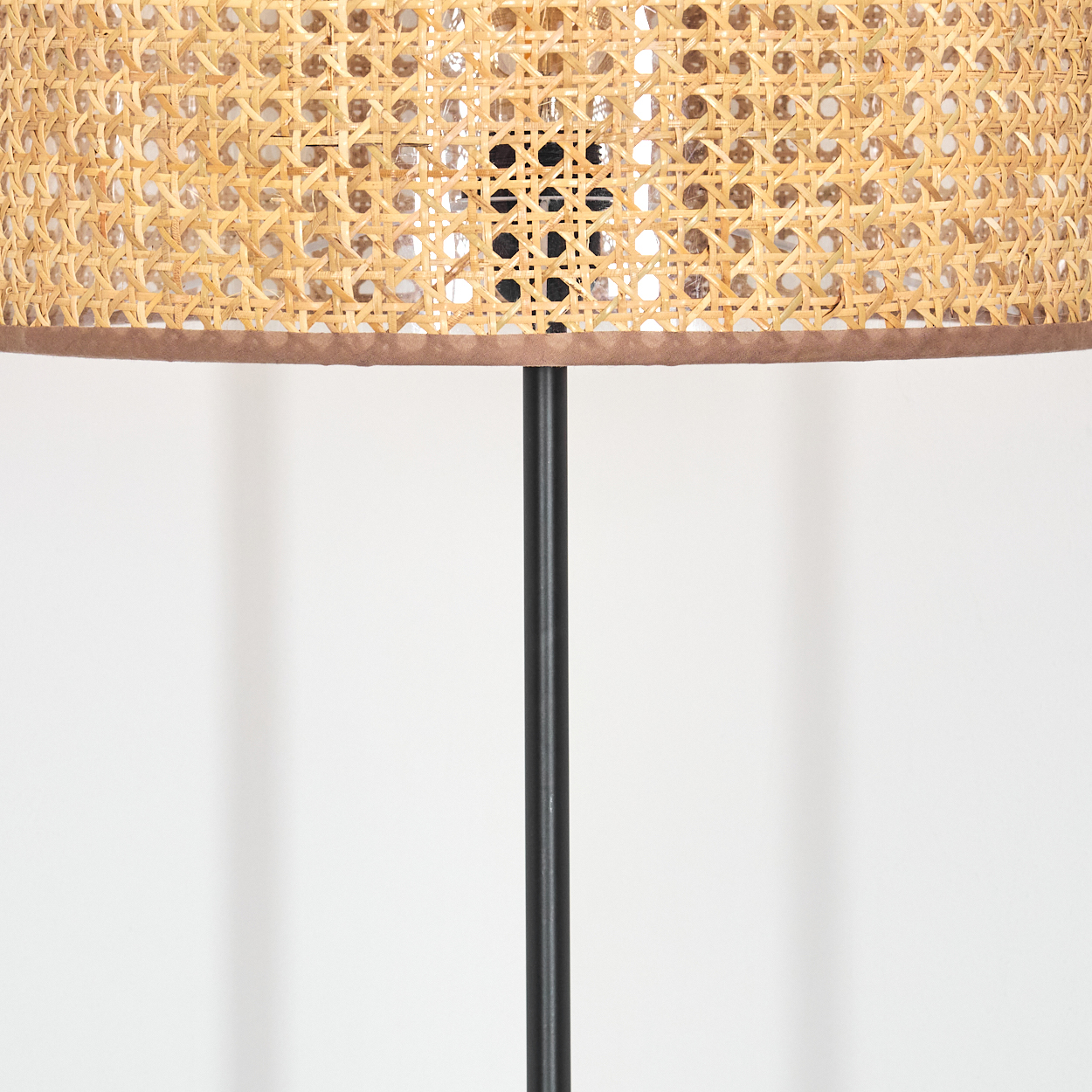 Nahaufnahme einer Lampe mit gewebtem Lampenschirm und schwarzem Metallständer. Der Hintergrund ist weiß.
