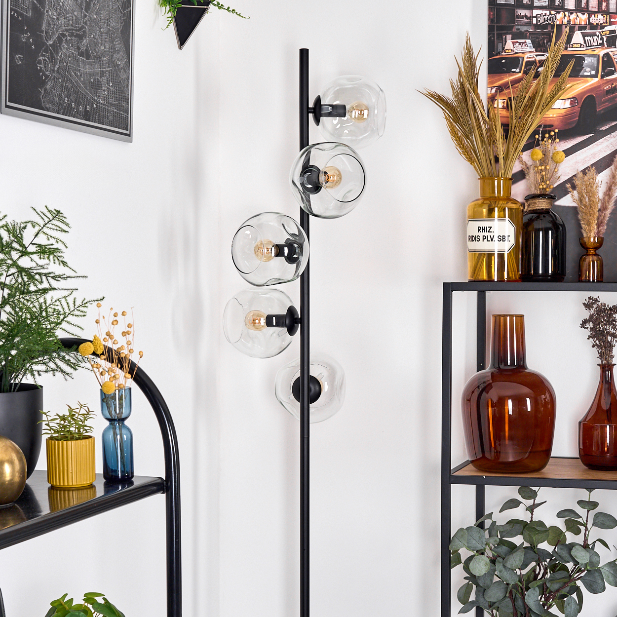 Ein modernes Wohnzimmer mit einer schwarzen Stehlampe mit Glaskugeln, Regalen mit Vasen und einer New York-Karte.