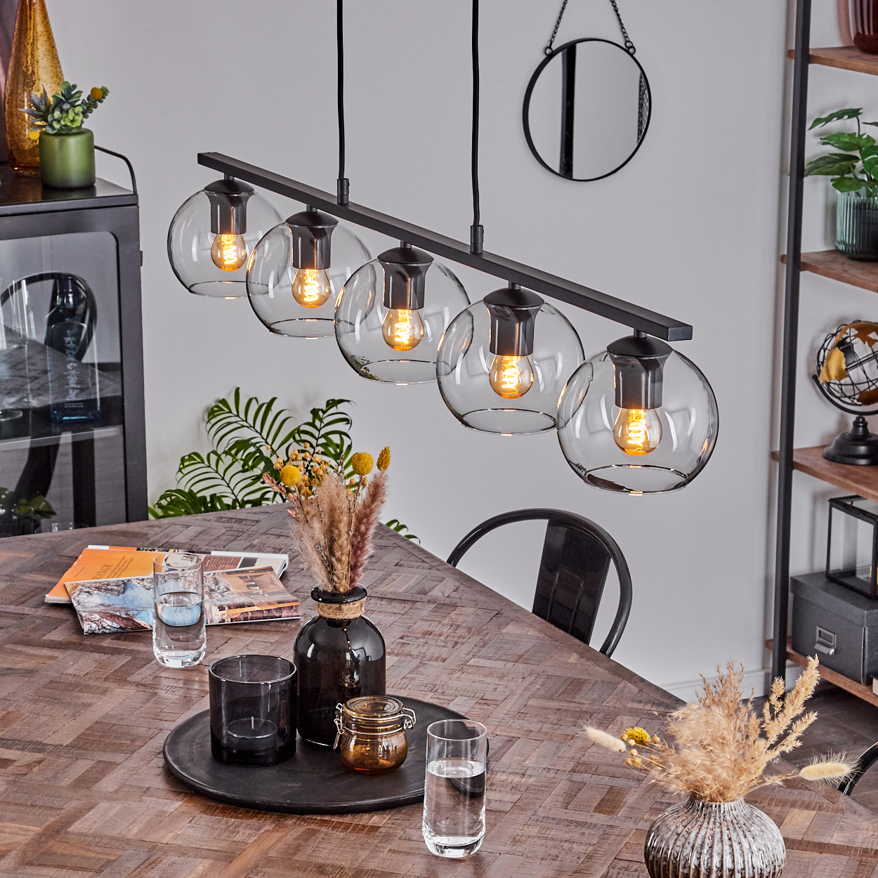 Esszimmer mit Holztisch, schwarzem Kronleuchter mit Glaskugeln und dekorativen Vasen.