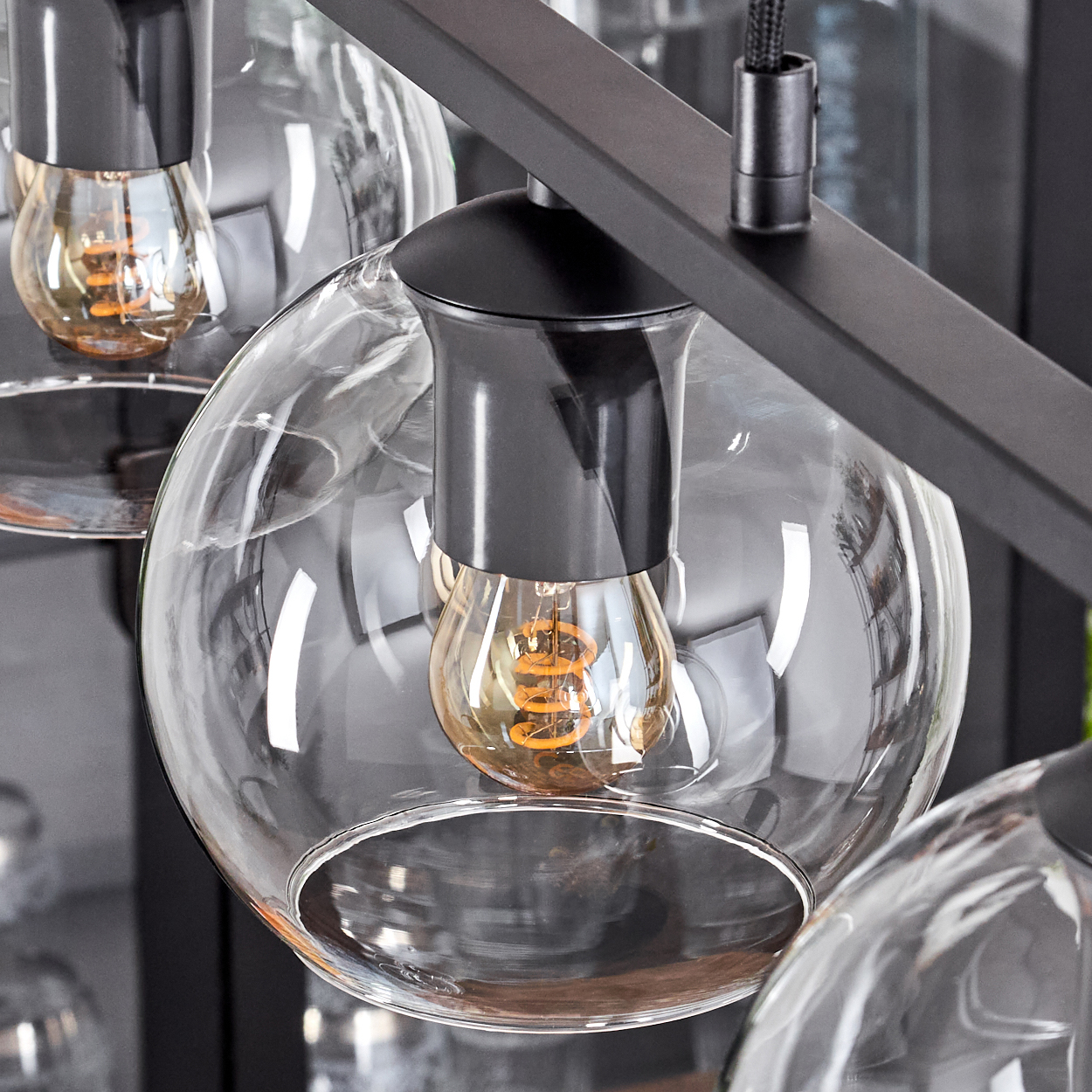 Nahaufnahme einer modernen Leuchte. Sie zeigt klare Glaskugeln mit warm getönten Glühbirnen, die vor einem schwarzen Metallrahmen angeordnet sind.