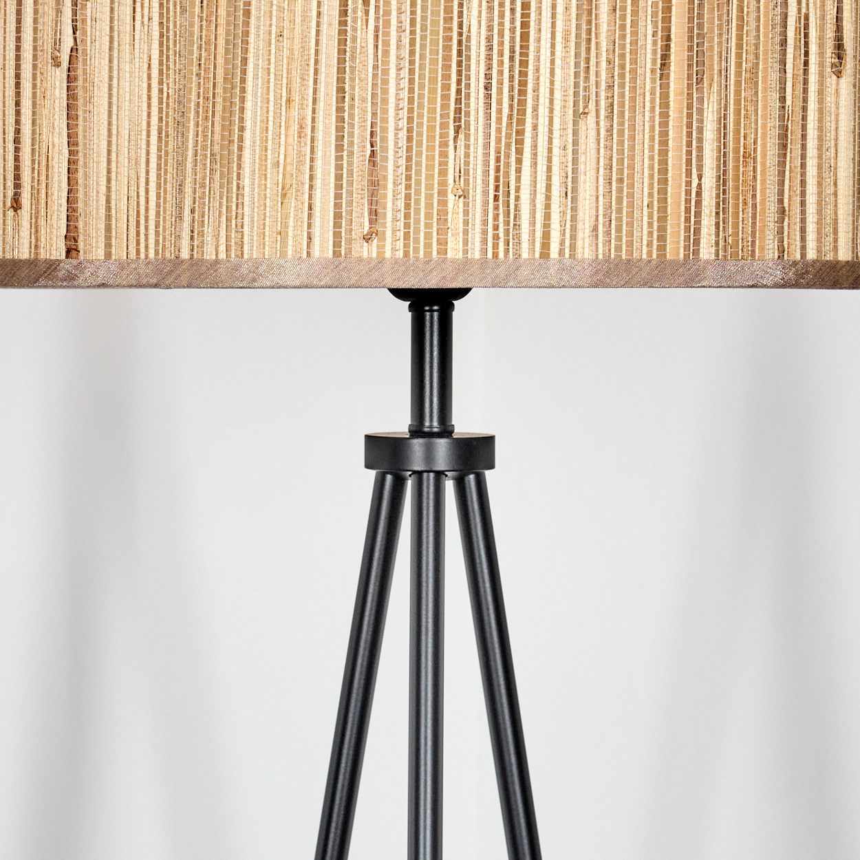 Nahaufnahme einer Lampe. Der Lampenschirm besteht aus gewebtem Stroh, über einem schwarzen Metall-Dreibein-Gestell.