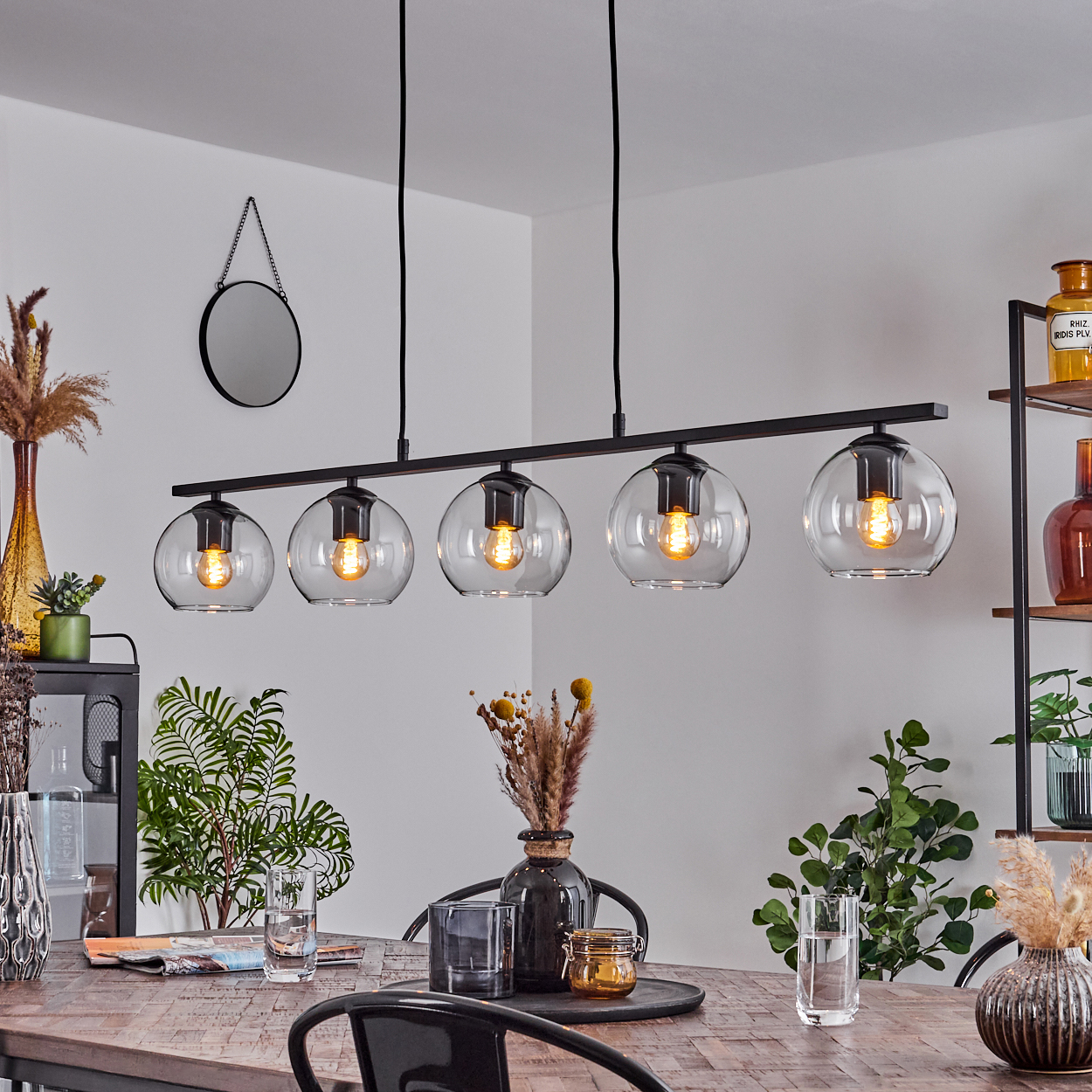 Esszimmer mit Holztisch, schwarzen Stühlen und einer schwarzen Leuchte mit fünf Glaskugelleuchten.