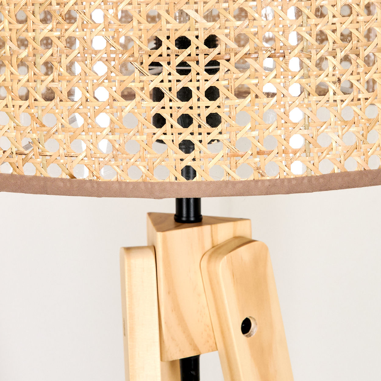 Nahaufnahme einer Lampe. Der Lampenschirm ist aus einem hellbraunen Material gewebt. Der Sockel besteht aus hellem Holz mit schwarzen Metallakzenten.