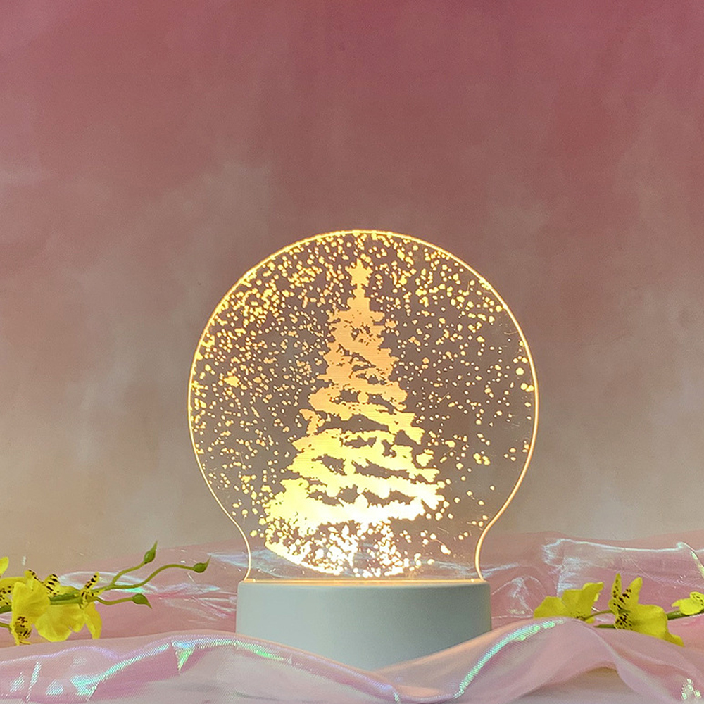 Eine leuchtende Weihnachtsbaumlampe auf weißem Sockel vor rosa Hintergrund. Gelbe Blumen und glänzender Stoff im Vordergrund.