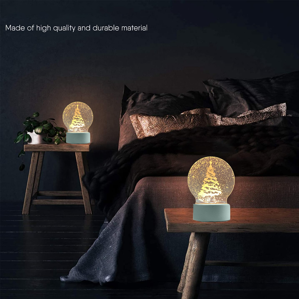 Zwei Schneekugel-Lampen mit Weihnachtsbäumen auf Nachttischen. Ein Bett mit Kissen und eine Pflanze sind ebenfalls sichtbar.