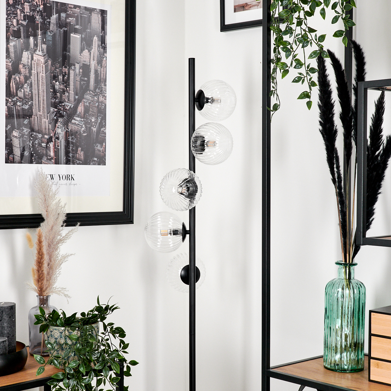 Ein modernes Wohnzimmer mit Stehlampe, New York-Bild und dekorativen Pflanzen in Vasen und Töpfen.