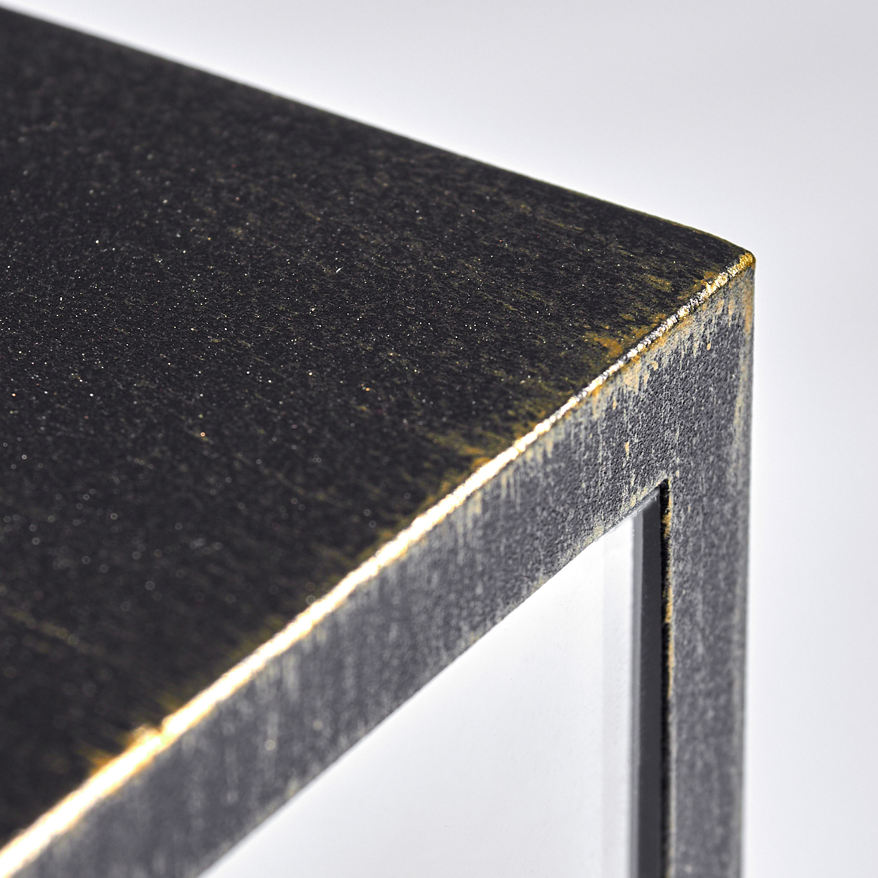 Nahaufnahme einer schwarzen und goldenen strukturierten Rahmenecke auf weißem Hintergrund. Der Rahmen hat ein raues, metallisches Aussehen.