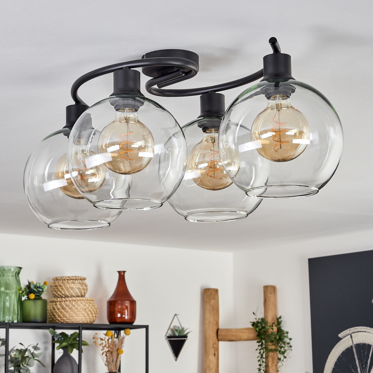 Eine moderne Deckenleuchte mit vier Glaskugeln. Jede Kugel hat eine Edison-Glühbirne. Schwarzer Metallrahmen. Weiße Decke.