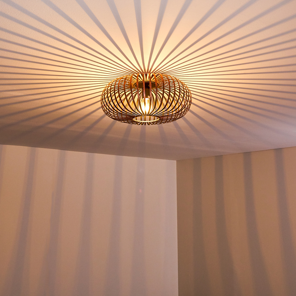 Eine dekorative Leuchte wirft radiale Schatten auf die Decke. Die Leuchte ist ein brauner, kugelförmiger Käfig mit einer zentralen Glühbirne.