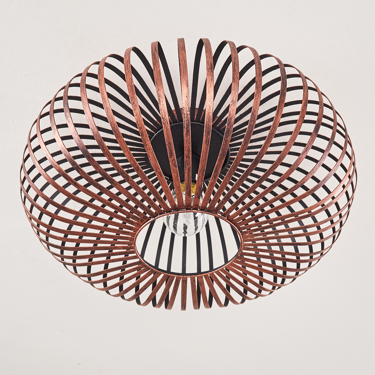 Eine kupferfarbene, kugelförmige Lampe mit einer Glühbirne in der Mitte hängt an einer weißen Decke.