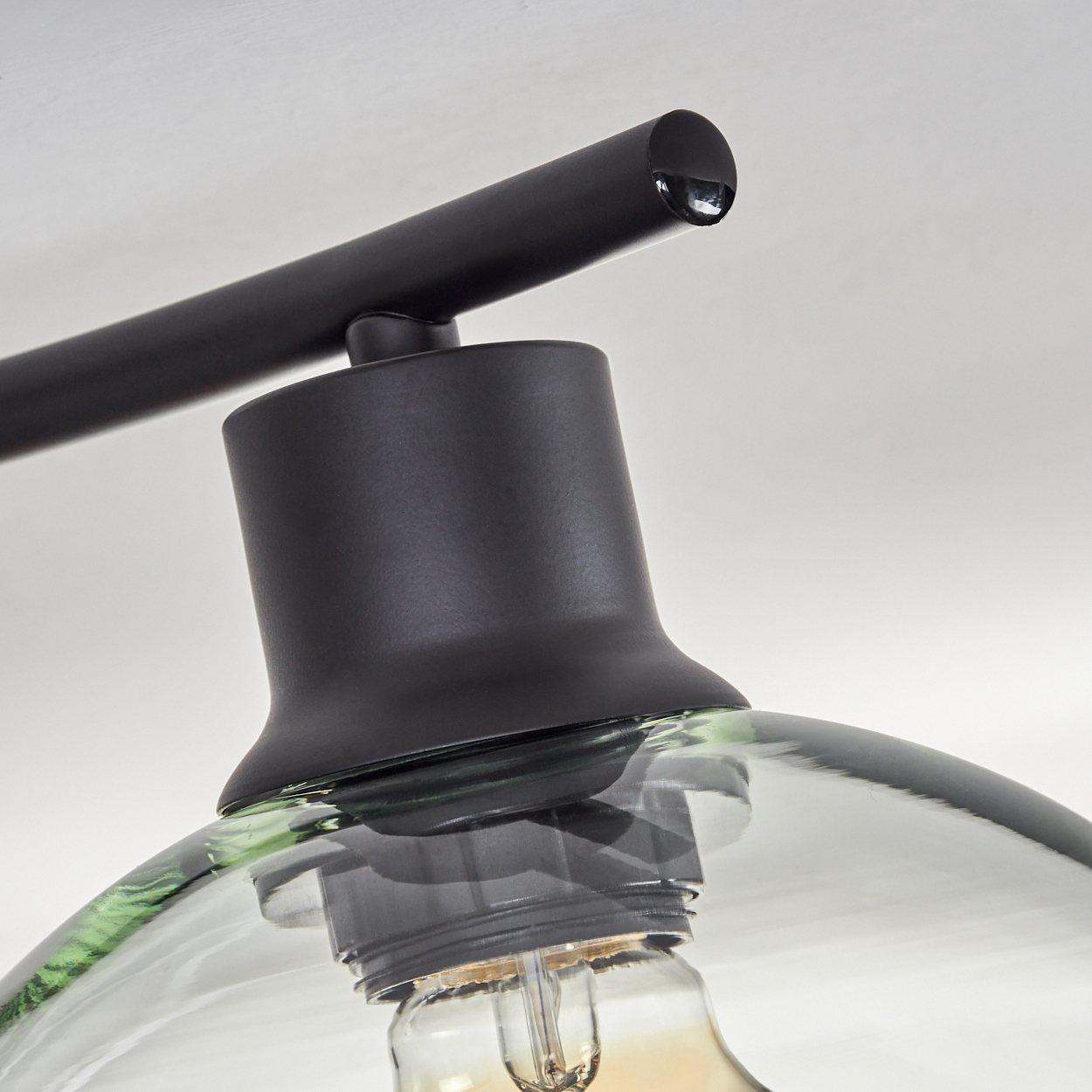 Nahaufnahme einer modernen Lampe. Sie hat einen schwarzen Arm, einen schwarzen Sockel und einen durchsichtigen Glasschirm mit Glühbirne.