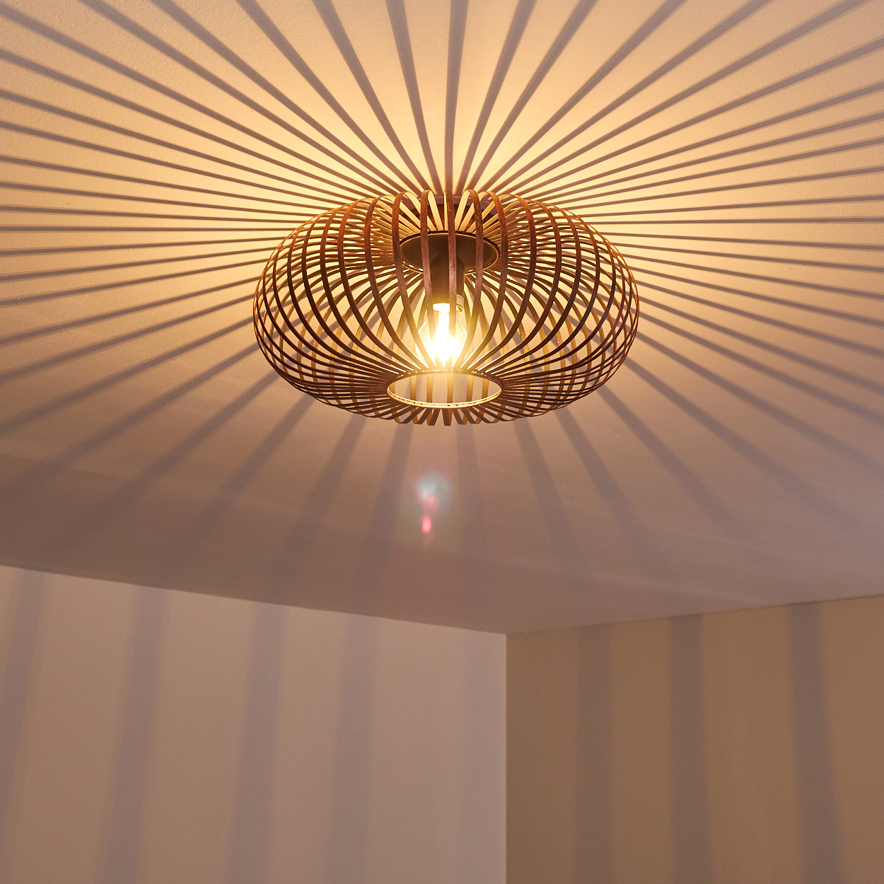 Eine dekorative Deckenlampe aus Holz wirft gestreifte Schatten auf die Decke. Die Lampe hat eine Glühbirne in der Mitte, die den Raum beleuchtet.