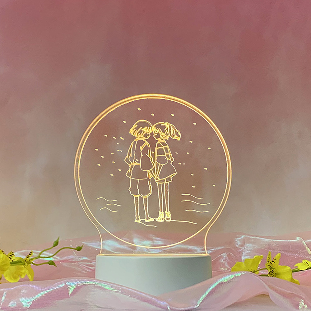 Eine leuchtende Lampe zeigt zwei Figuren in einem Kreis. Gelbe Blumen und rosa Stoff befinden sich im Vordergrund, mit rosa Wolken im Hintergrund.